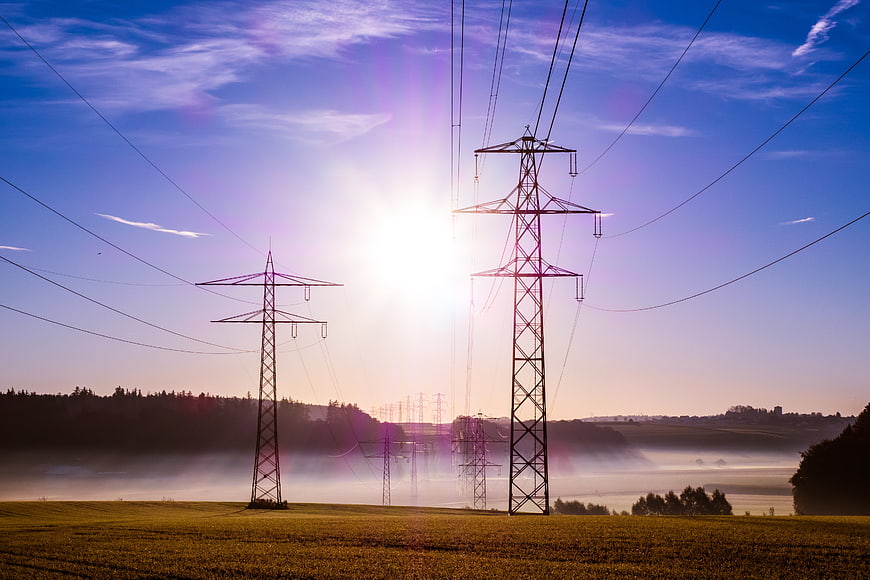 Electricity pylons in misty field at sunrise