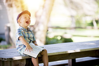 Laughing Boy Reading Book on Wooden Bench Outdoors