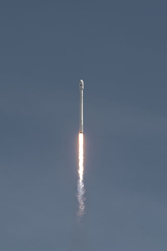 SpaceX Falcon 9 rocket launch with bright exhaust trail against clear blue sky