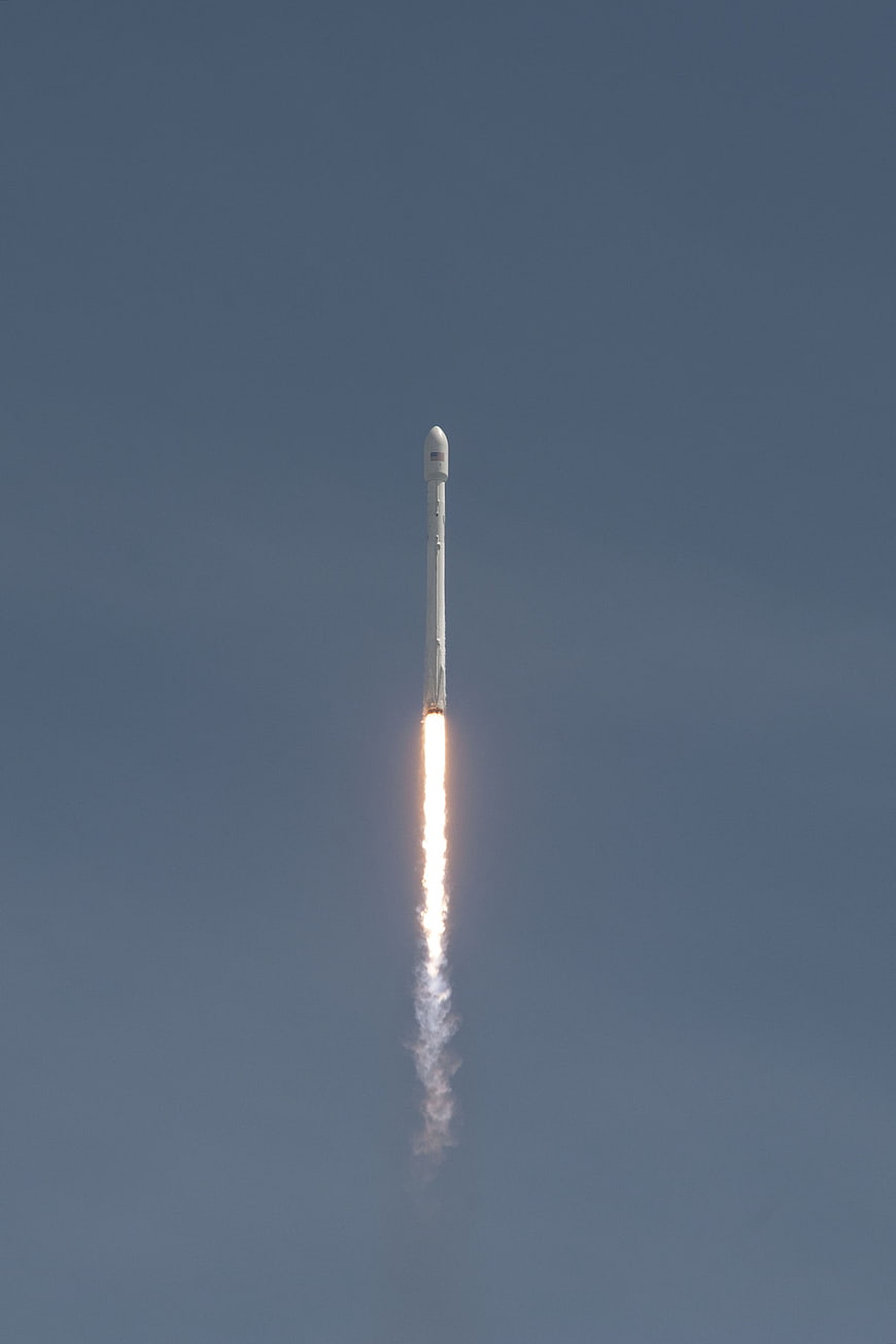 SpaceX Falcon 9 rocket launch with bright exhaust trail against clear blue sky