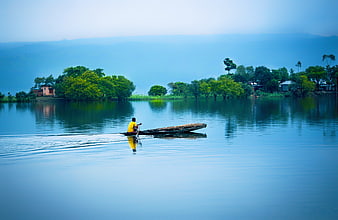 Man in yellow shirt rowing a wooden boat on a calm blue lake