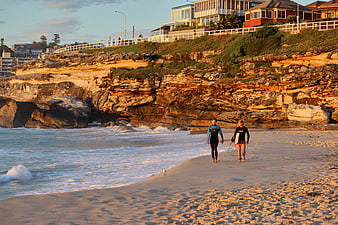 Surfers walking on sandy beach at sunset with cliffs