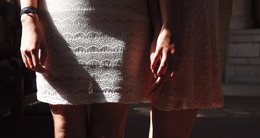 Two women holding hands in lace dresses in sunlight