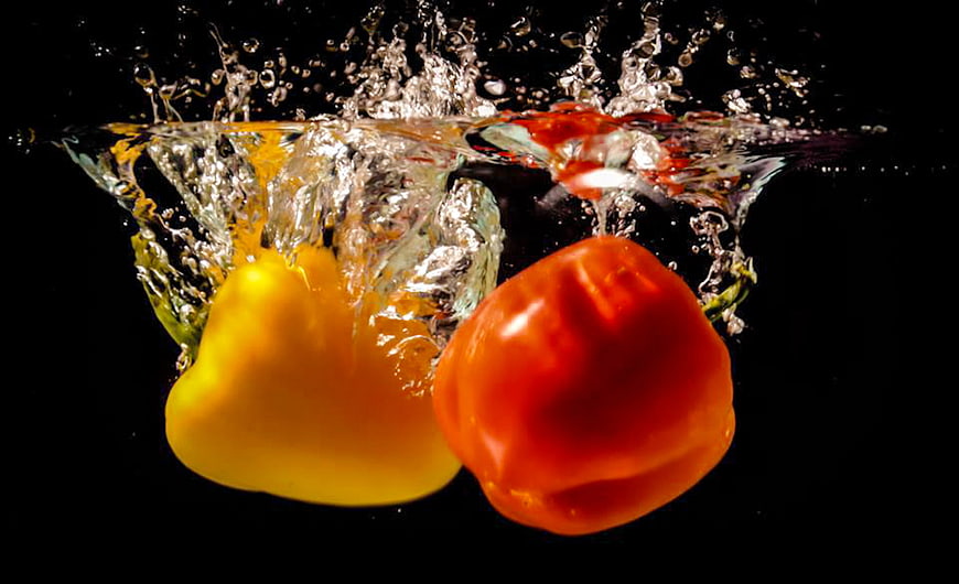 Red and yellow bell peppers splashing into water