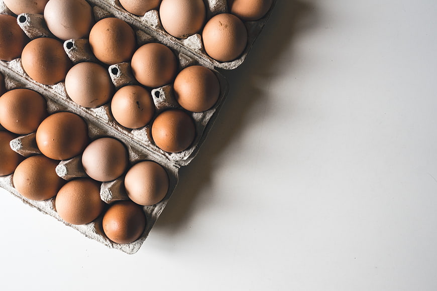Top View of Brown Eggs in Cardboard Tray on White Background