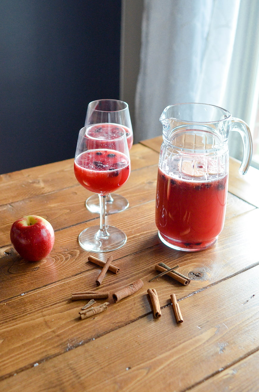 Pitcher of red cranberry punch with cinnamon sticks on wooden table