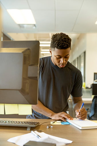 Focused young man writing in notebook at office desk