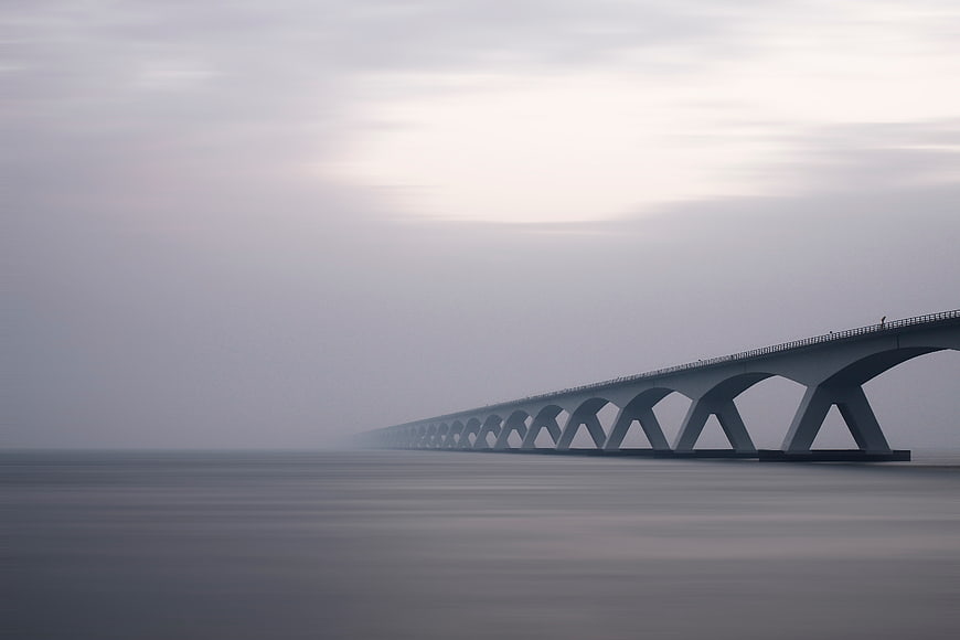 Long concrete bridge disappearing into foggy sea horizon