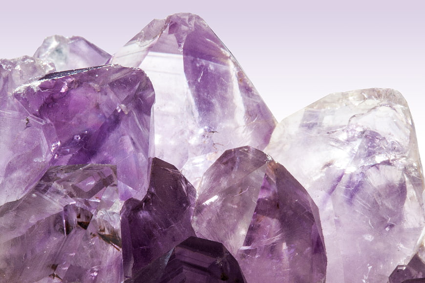 Close-up of raw purple amethyst crystal cluster on white background