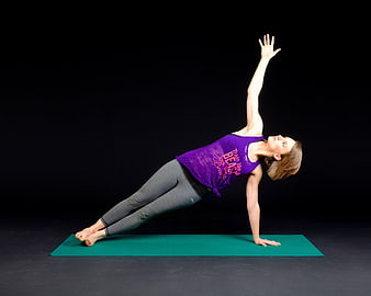 Woman performing side plank yoga pose on green mat