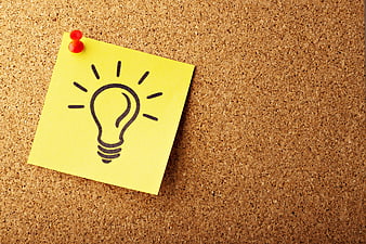 Yellow sticky note with lightbulb drawing on cork board