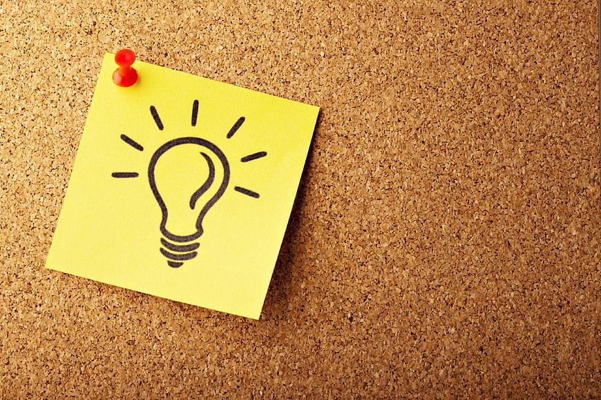 Yellow sticky note with lightbulb drawing on cork board