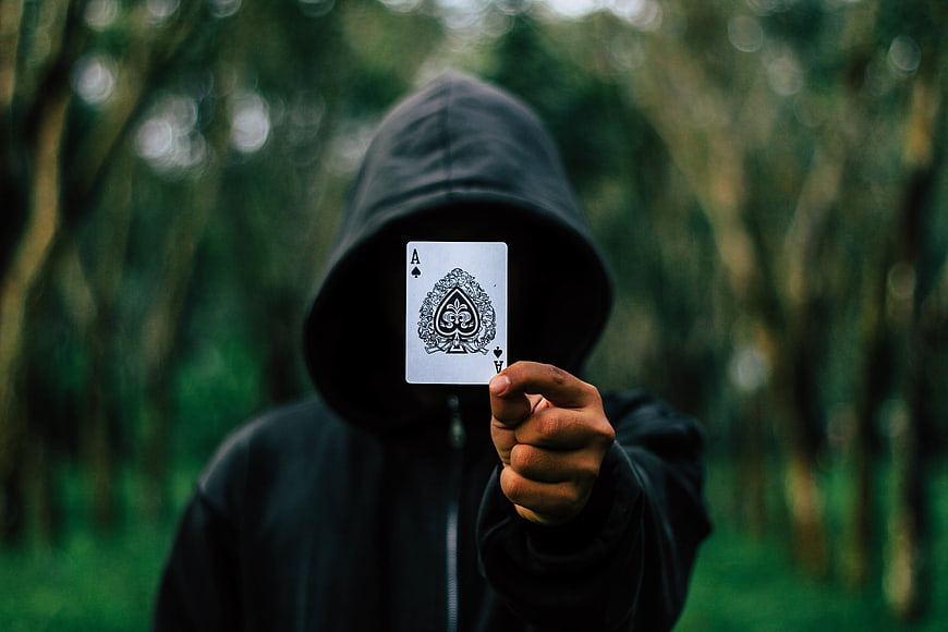 Mysterious hooded figure holding Ace of Spades in forest