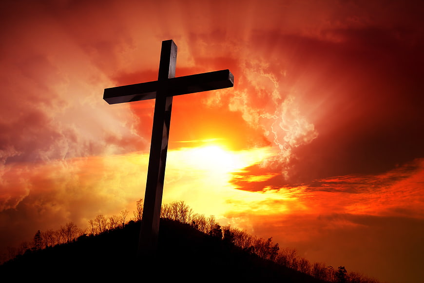 Silhouette of Cross on Hilltop Against Dramatic Sunset