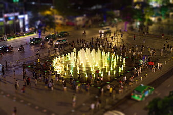 Tilt-shift night view of illuminated fountain with crowd