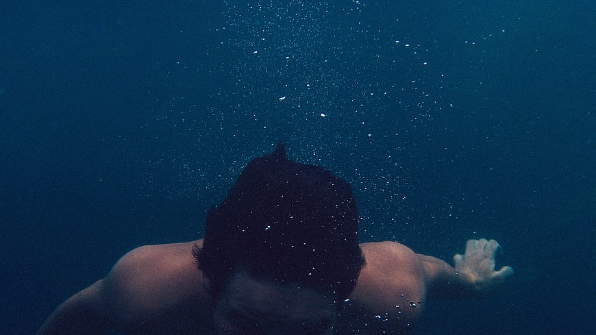 Underwater shot of man swimming with rising bubbles