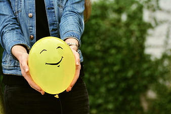 Woman holding yellow smiley balloon outdoors