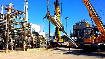 Heavy industrial crane lifting pipes at refinery plant