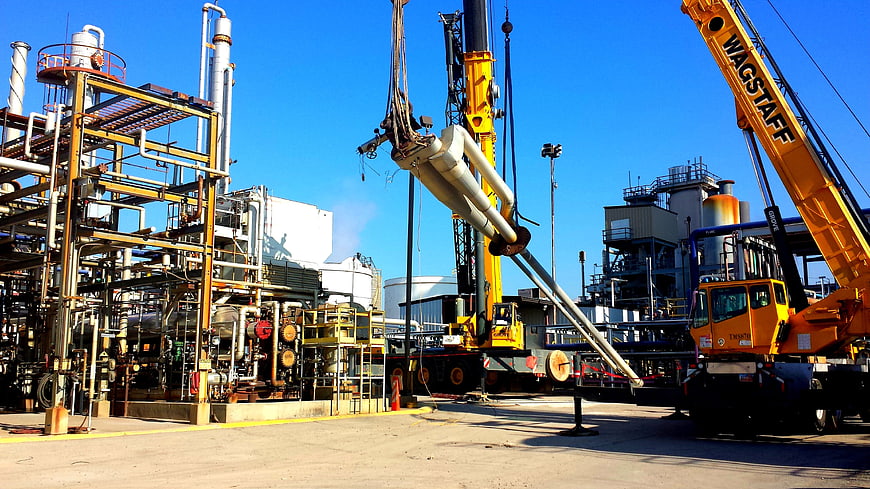 Heavy industrial crane lifting pipes at refinery plant