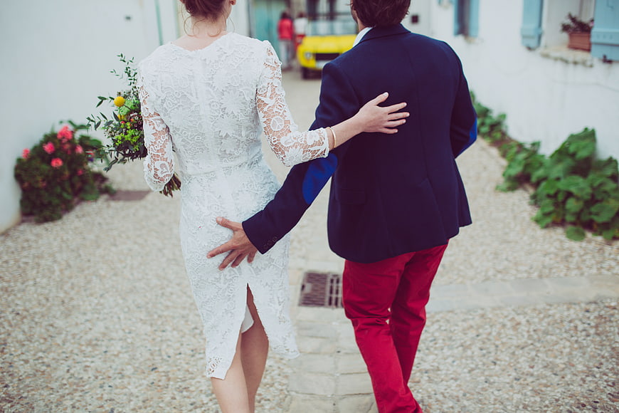 Couple walking away in white lace dress and red trousers