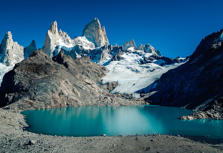 Turquoise glacial lake with jagged mountain peaks and hikers
