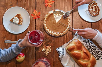 Top view of autumn table with pumpkin pie, bread, and hands