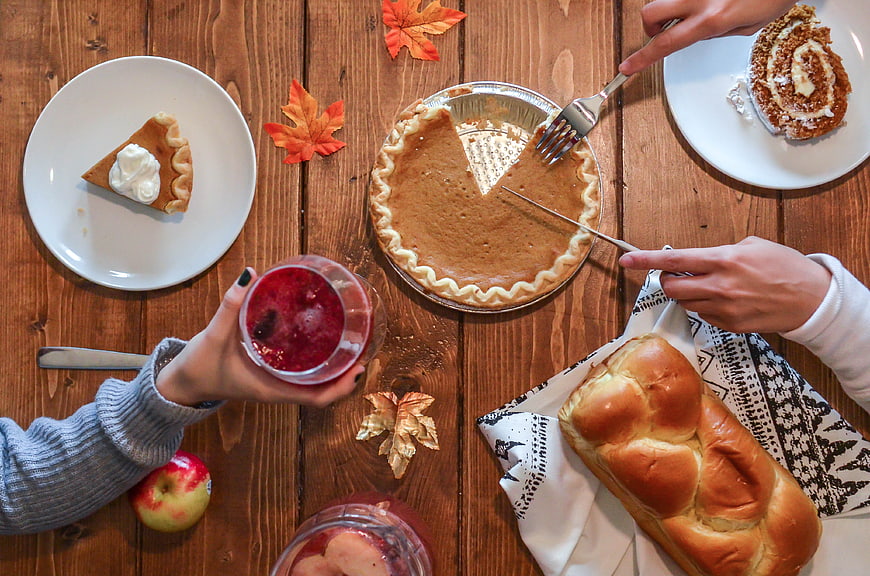Top view of autumn table with pumpkin pie, bread, and hands