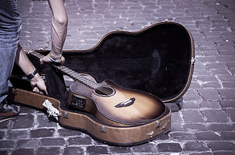 Musician placing acoustic guitar in vintage case on cobblestones