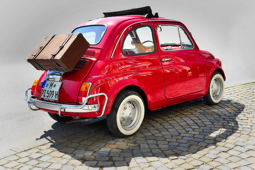 Rear View Of Red Vintage Fiat 500 With Vintage Suitcase On Cobblestone