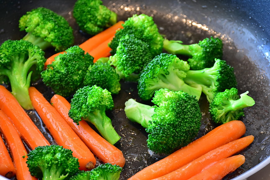 Fresh broccoli and carrots cooking in a frying pan