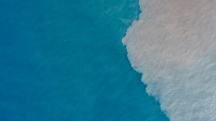 Aerial view of turquoise ocean waves crashing on white sand