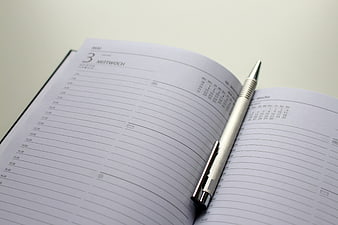 Open Weekly Planner Notebook with Silver Pen on Desk