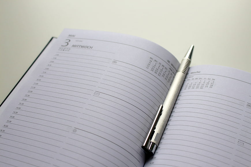 Open Weekly Planner Notebook with Silver Pen on Desk