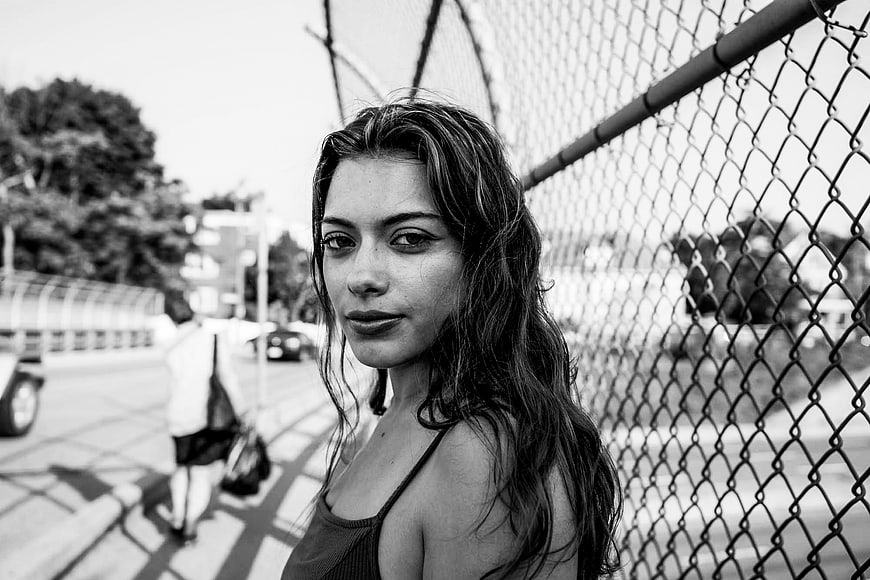 Black and white portrait of young woman by chain link fence