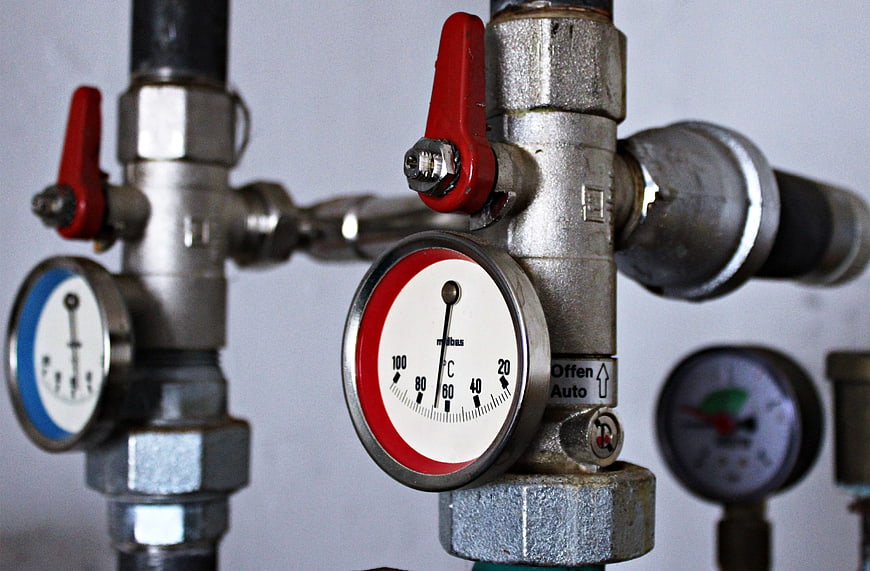 Close-up of heating system pipes with temperature gauge and red valves