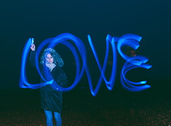 Woman writing LOVE with blue light painting at night