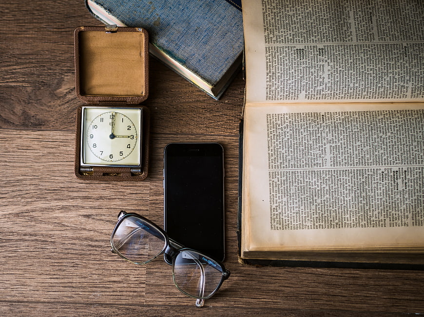 Vintage pocket watch, smartphone, and open book on wooden desk