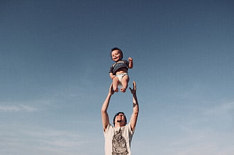 Father tossing baby into the air against blue sky