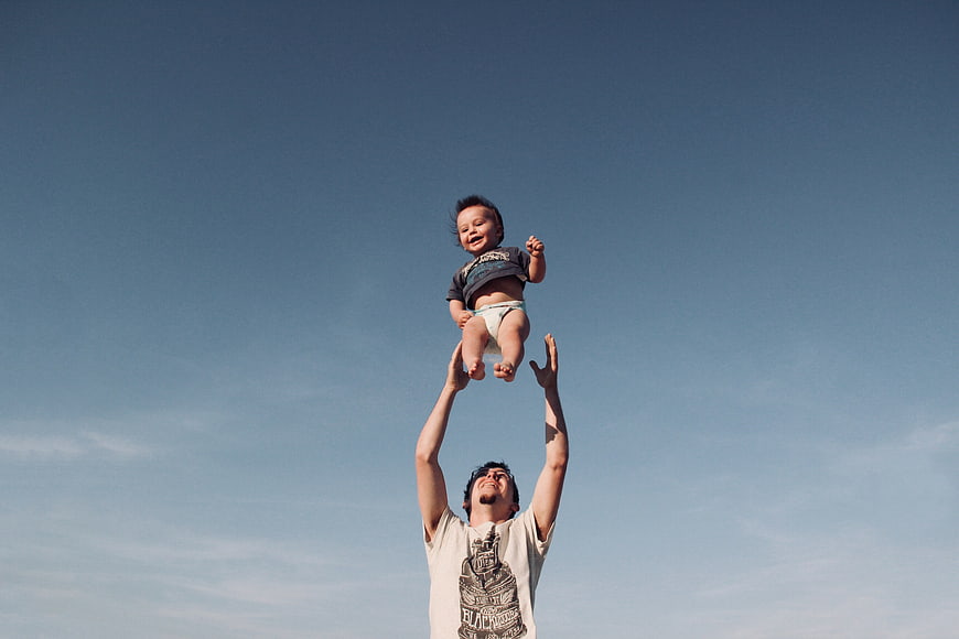 Father tossing baby into the air against blue sky