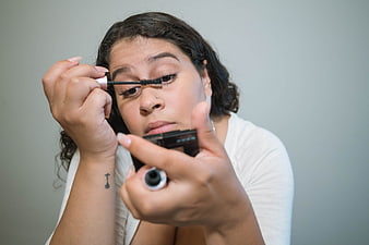 Woman applying mascara while looking in a compact mirror
