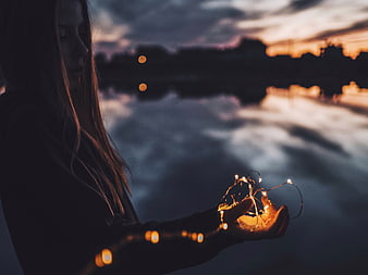 Woman holding fairy lights by lake at dusk