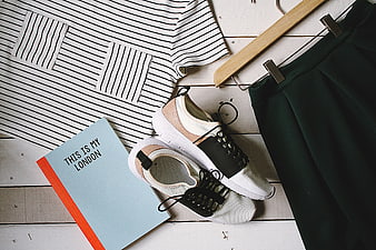 Flat lay of striped shirt, sneakers, skirt, and book on white wood