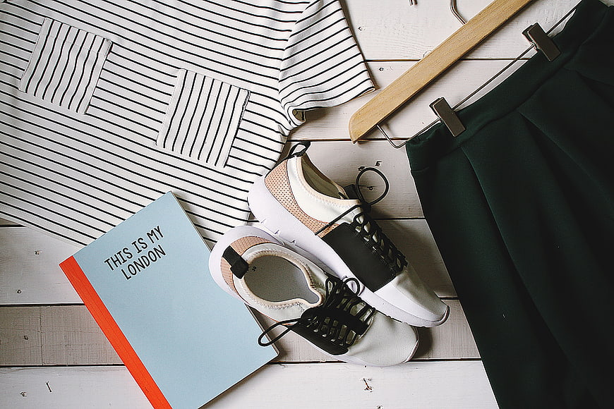 Flat lay of striped shirt, sneakers, skirt, and book on white wood