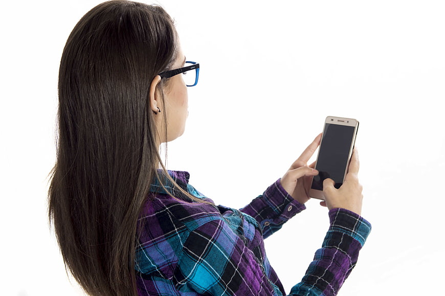 Young woman with glasses using smartphone on white background