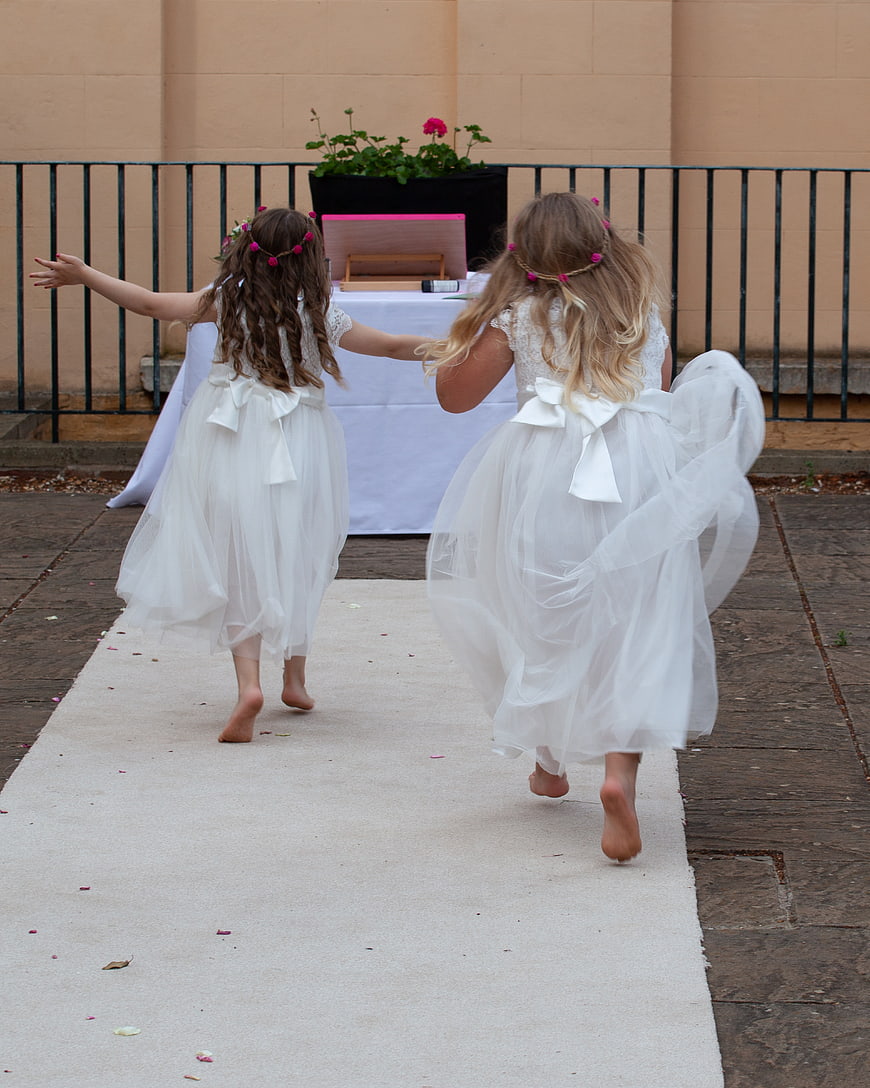 Two young flower girls running down a wedding aisle