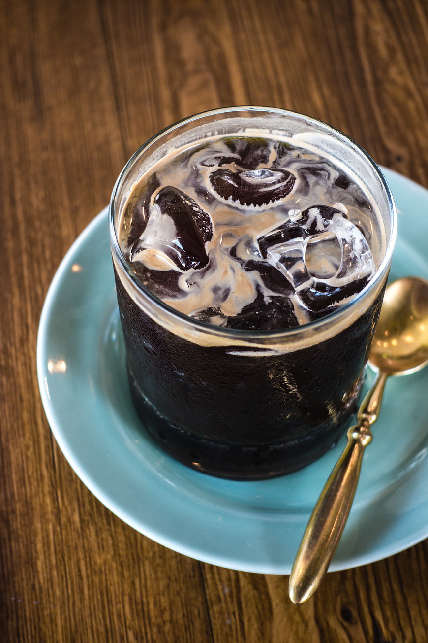 Overhead view of iced black coffee with milk swirls on wooden table