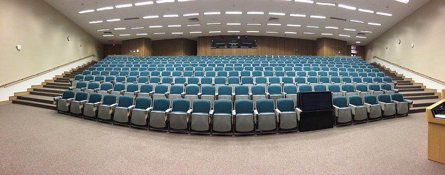 Empty University Auditorium With Rows Of Blue Seating And Wooden Stage
