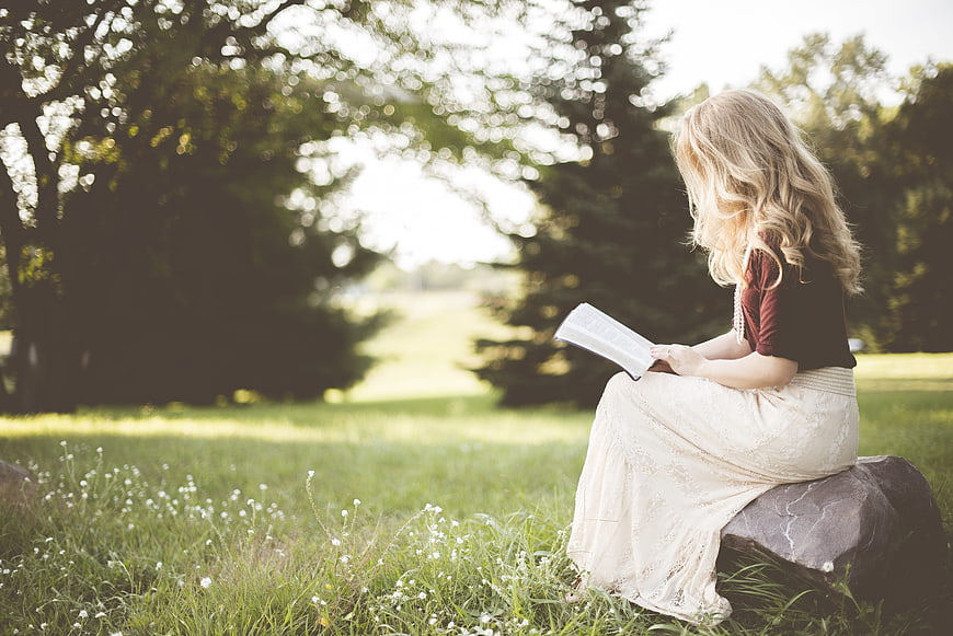 Young Blonde Woman Reading Book Outdoors in Nature