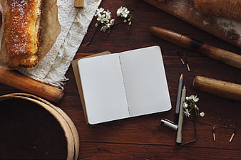 Open blank notebook with bread and baking tools on wooden table