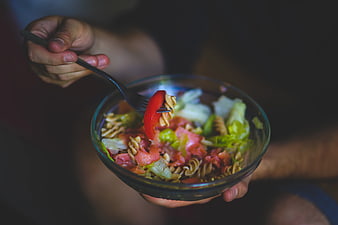 Close-up of hands eating healthy pasta salad with vegetables